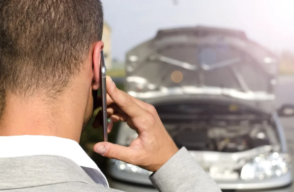 Man standing by the broken vehicle calling tow service